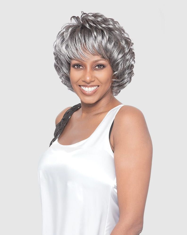 A woman smiles wearing the Vanessa JETTY Synthetic Wig: a short, voluminous silver-grey curly bob with bangs.