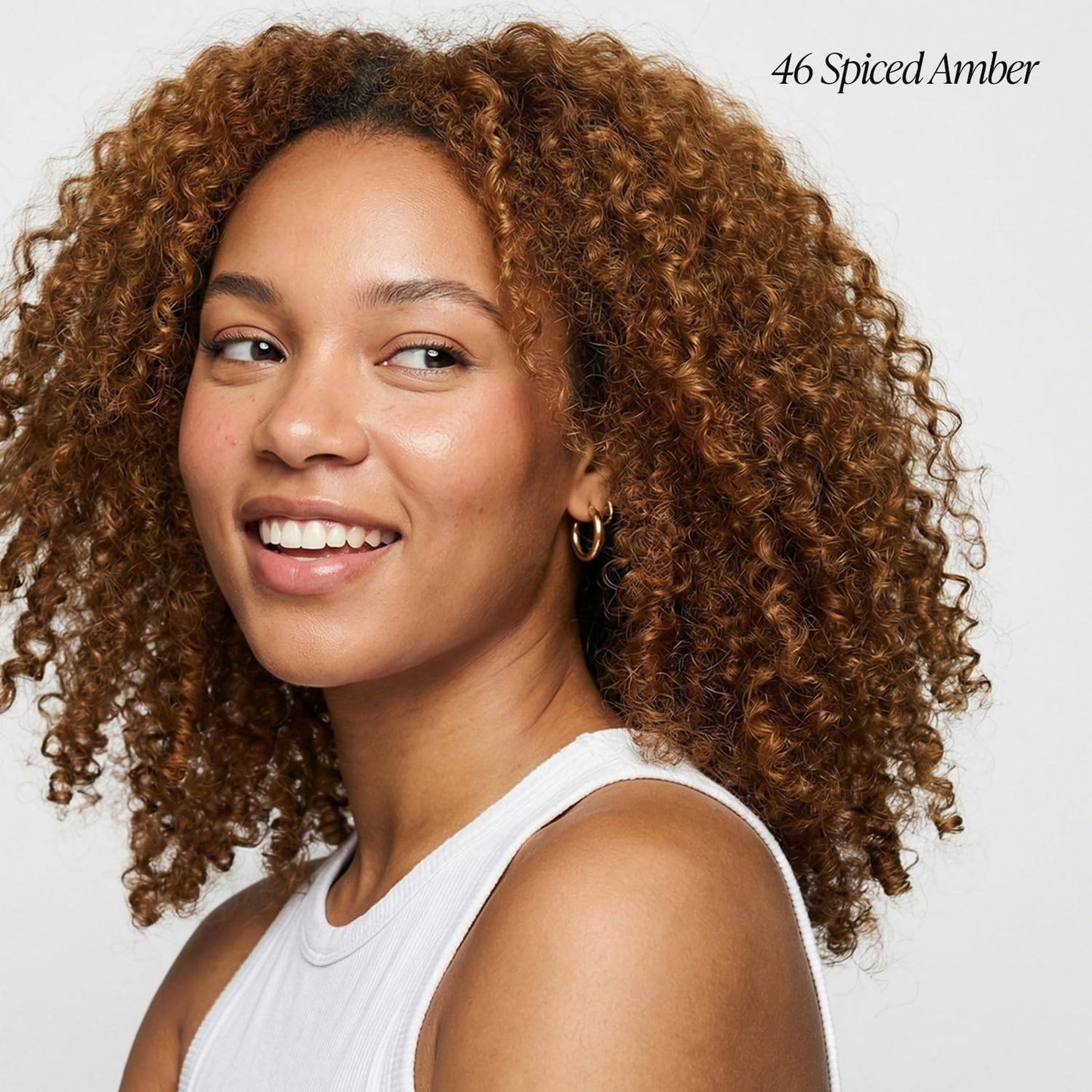 Woman with voluminous, shoulder-length curls in Creative Image Adore #46 Spiced Amber hair color, smiling.