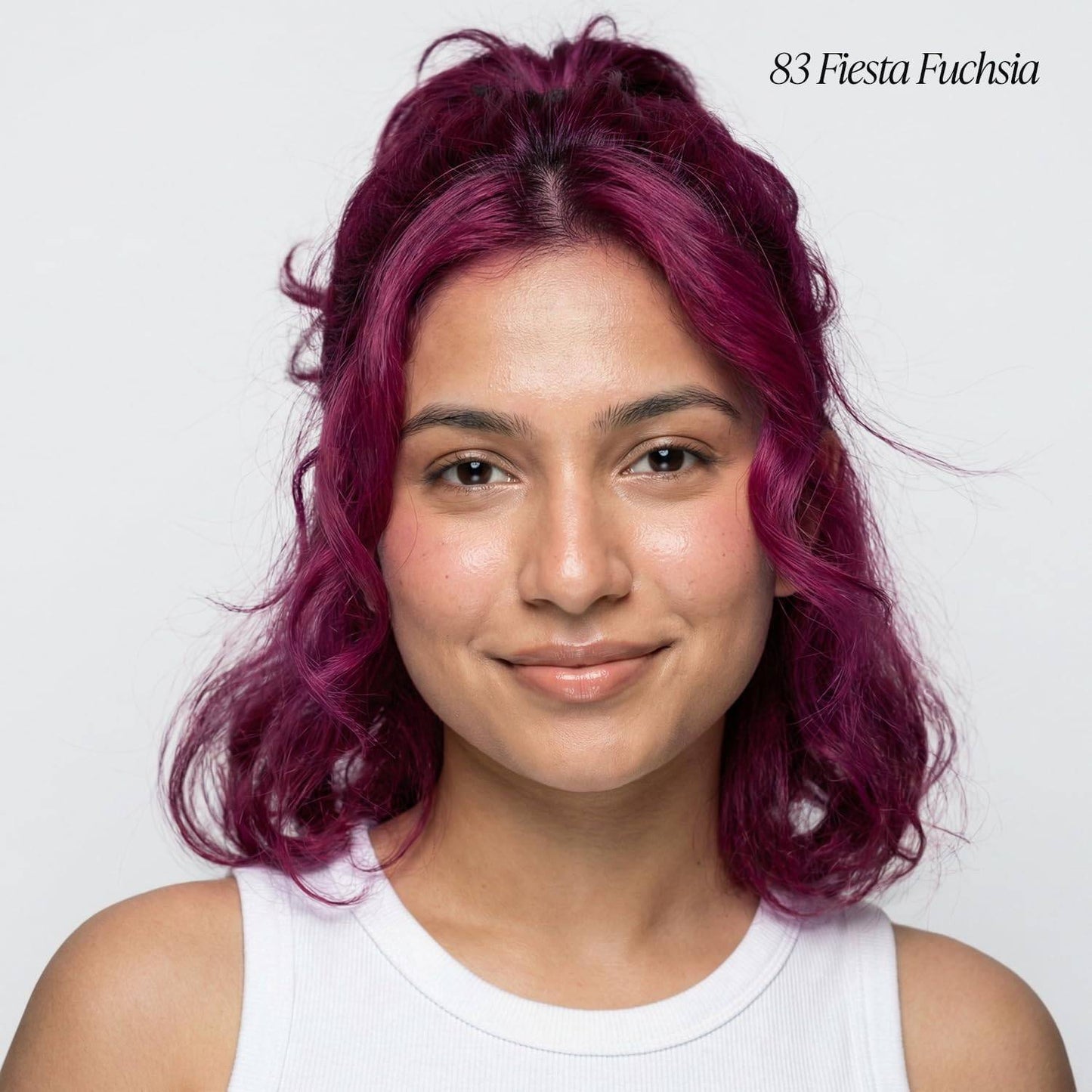 Smiling woman with wavy, shoulder-length, vibrant fuchsia hair styled in a messy half-updo, showcasing Adore #83 Fiesta Fu...