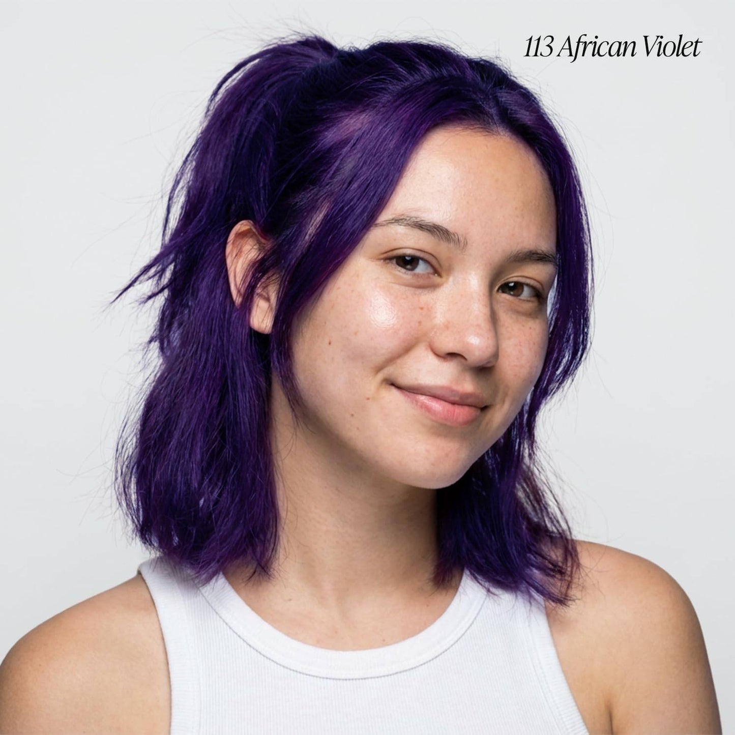 Smiling woman with shoulder-length, layered hair in vibrant Adore African Violet semi-permanent hair color.