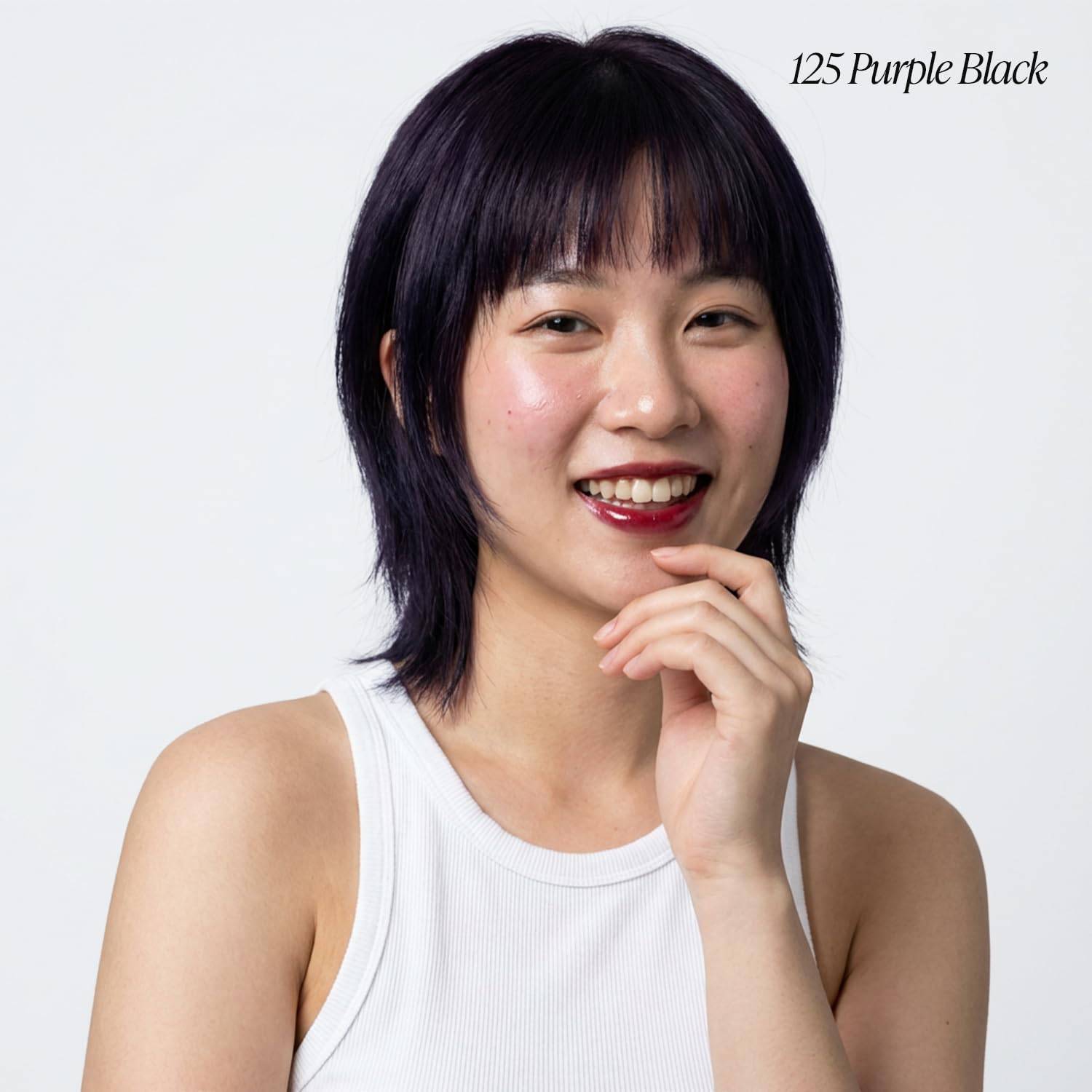 Smiling woman models Creative Image Adore Semi-Permanent Hair Color #125 Purple Black, with short, layered purple-black ha...