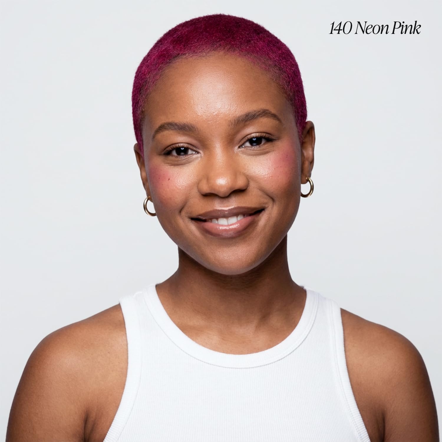 Smiling person models Adore #140 Neon Pink semi-permanent hair color in a very short, vibrant buzz cut.