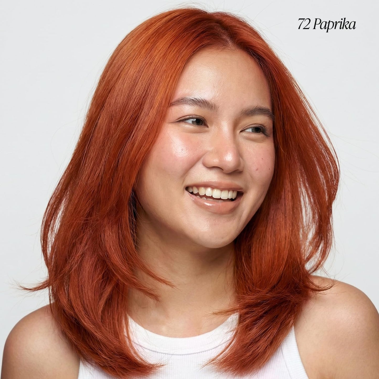 A smiling woman models medium, layered Creative Image Adore #072 Paprika hair, styled with subtle outward flicks.
