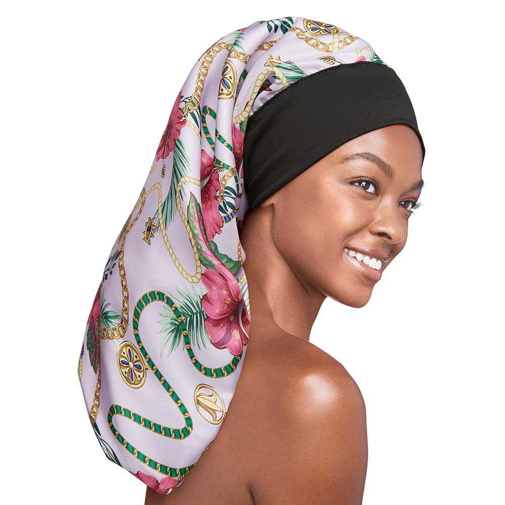 Smiling woman models a RED By Kiss Luxury Satin Wide Edge Braid Bonnet, featuring a vibrant floral and chain pattern.