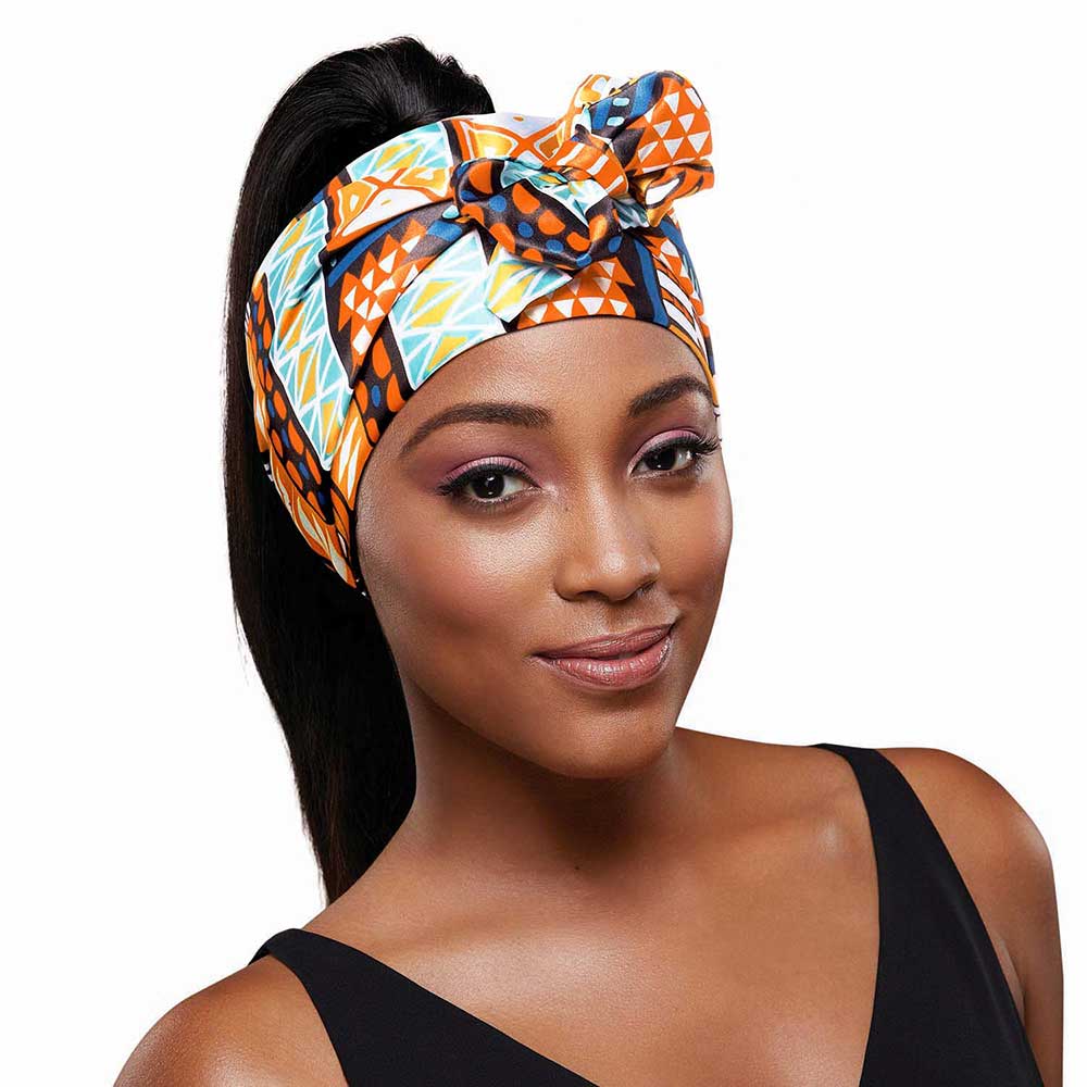 Woman wearing RED By Kiss Edge Laying Scarf (AZTEC) with a colorful geometric pattern; dark hair styled in a high ponytail.