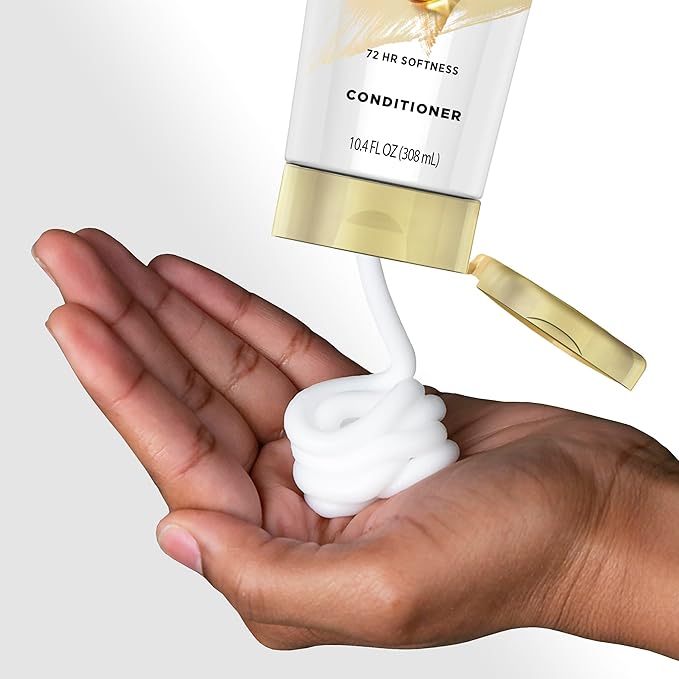 Pantene Pro-V conditioner squeezing out of its gold-capped tube into a hand, revealing a thick white cream.