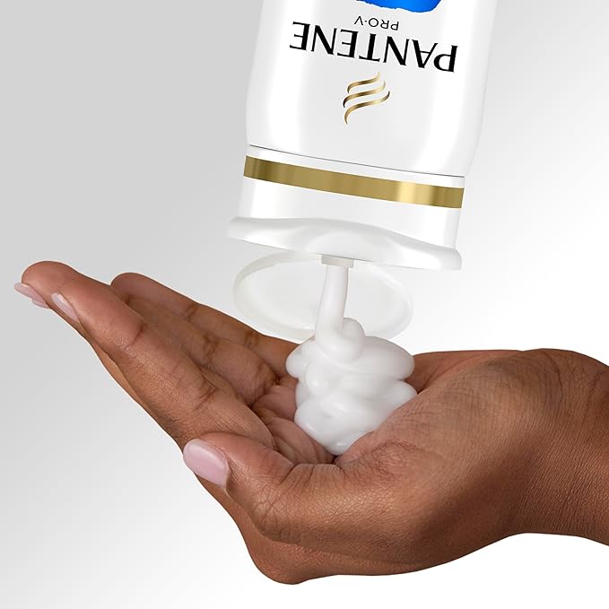 Dark-skinned hand catching white, foamy Pantene Pro-V Repair & Protect Shampoo dispensed from an inverted bottle.