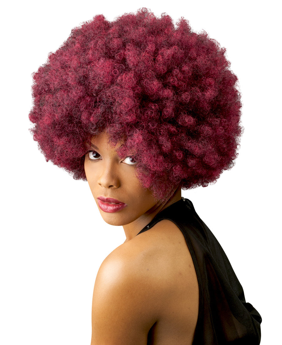 A woman models the New Born Free CUTIE 52 Wig, featuring a vibrant red, short, and very full curly afro style.