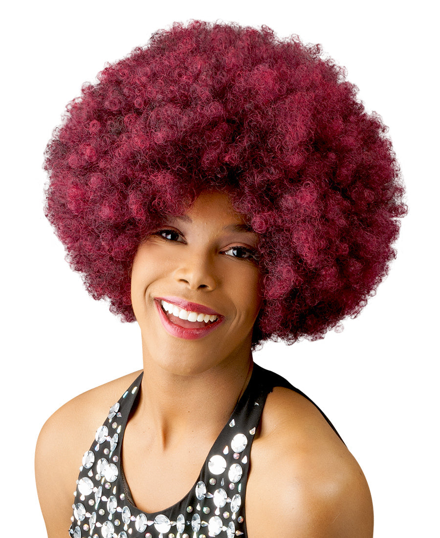 A woman smiles, wearing the New Born Free CUTIE 52 Wig, a short, full, bright red curly afro.